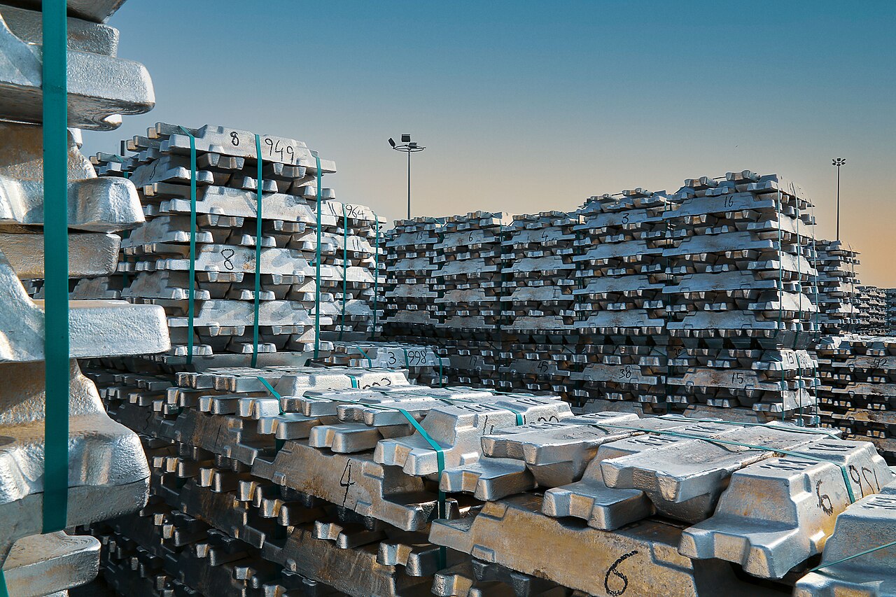 Real photograph of stacked aluminum ingots at an industrial storage yard